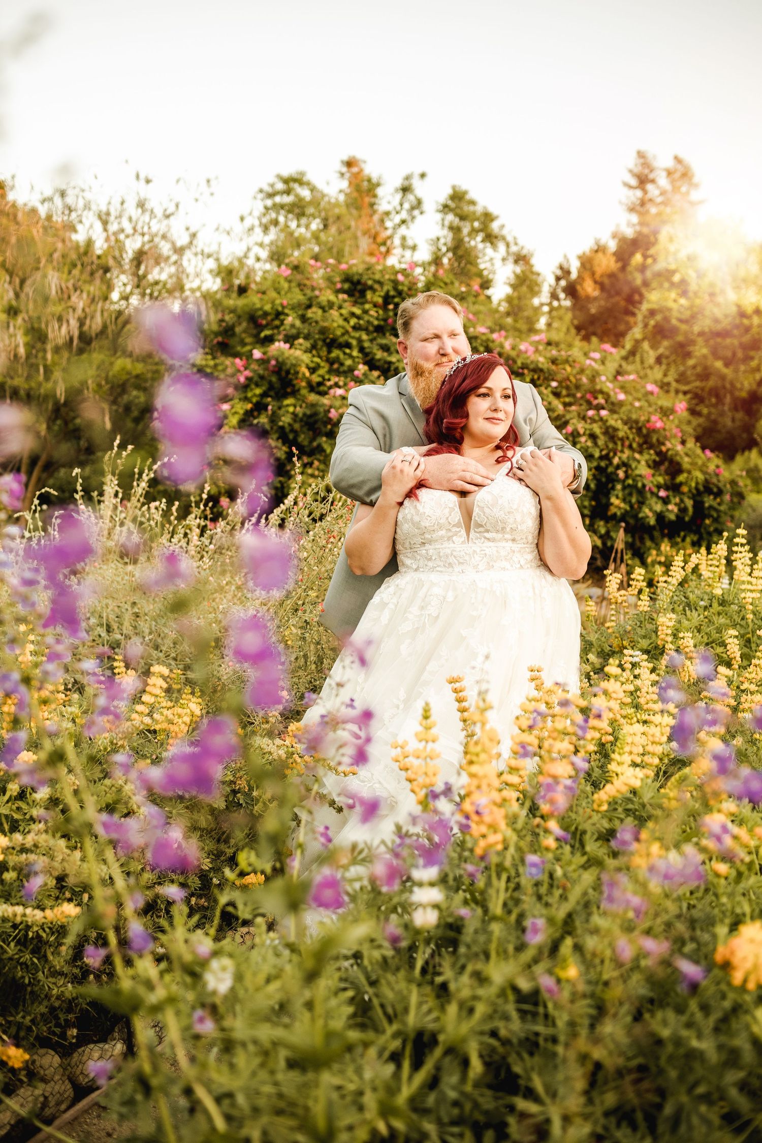 A couple embraces in a wildflower meadow during golden hour.