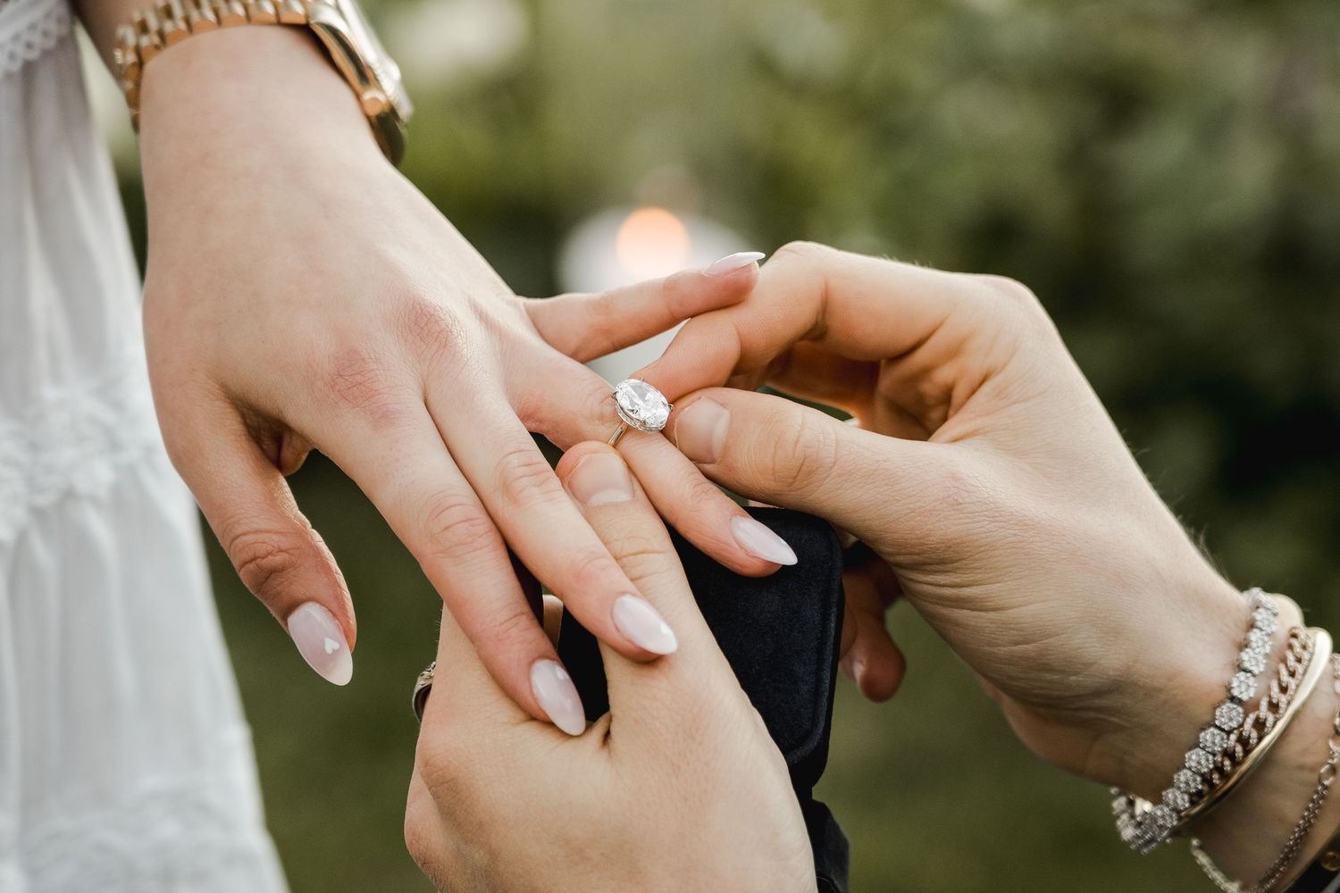 Close-up of hands placing engagement ring on finger with elegant jewelry details.