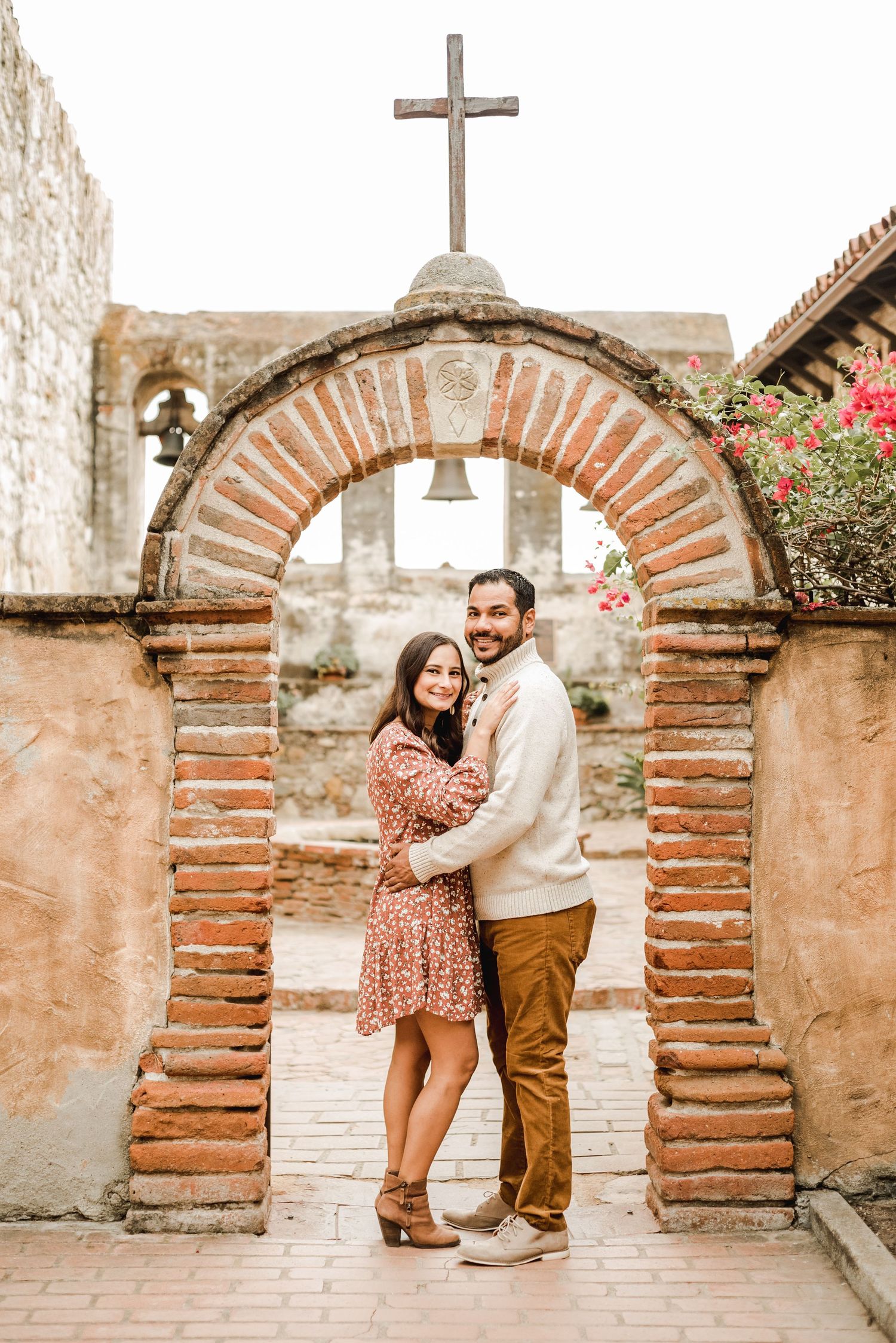 A romantic photoshoot at a rustic mission with brick archways and a cross in the background.