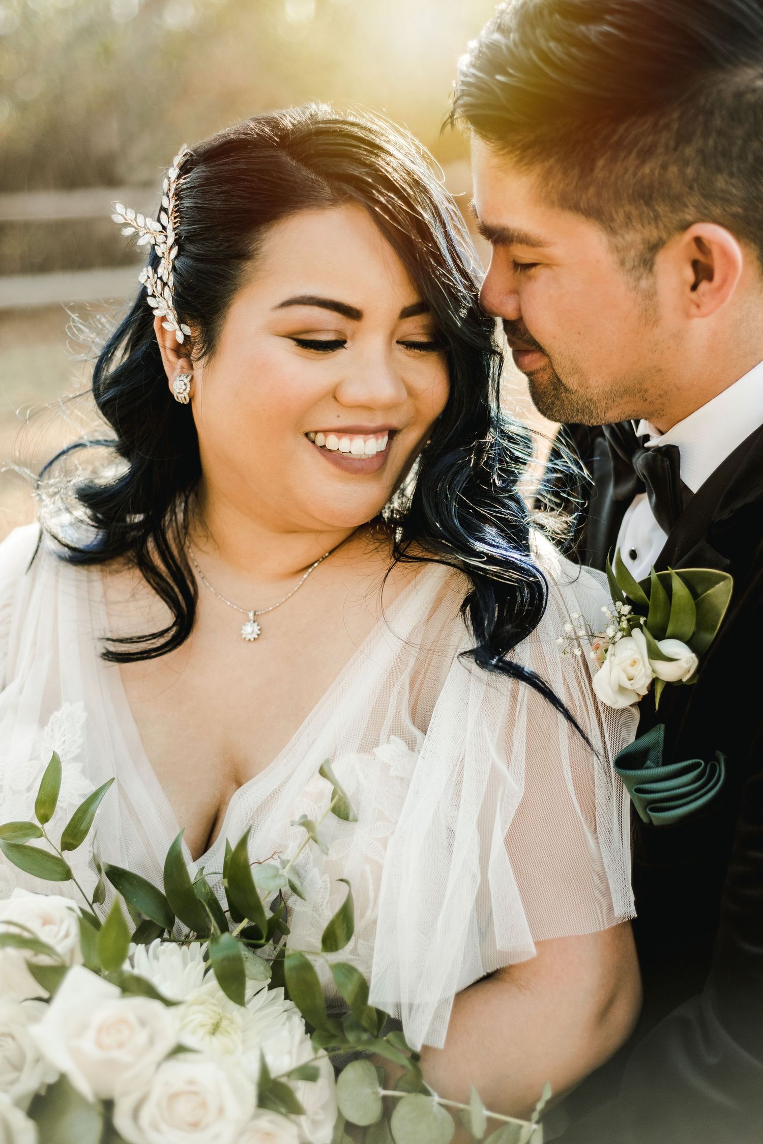 Intimate wedding portrait of newlyweds sharing a tender moment with white roses and greenery bouquet.