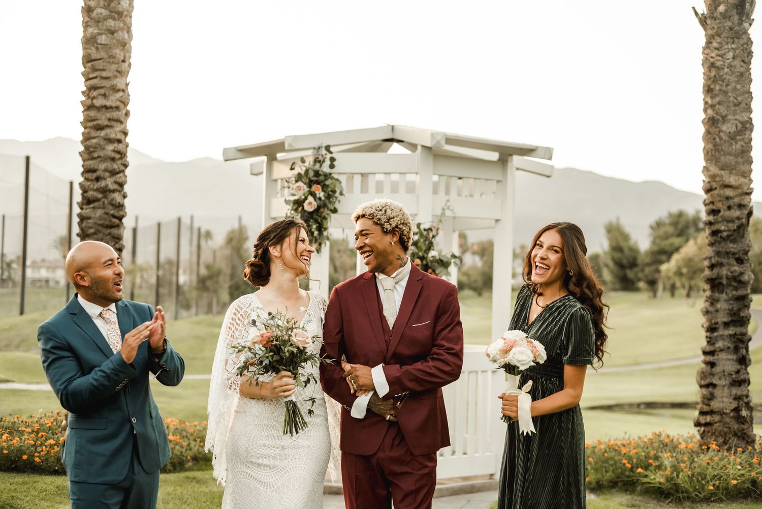 Wedding party celebrating outdoors with palm trees and building in background.