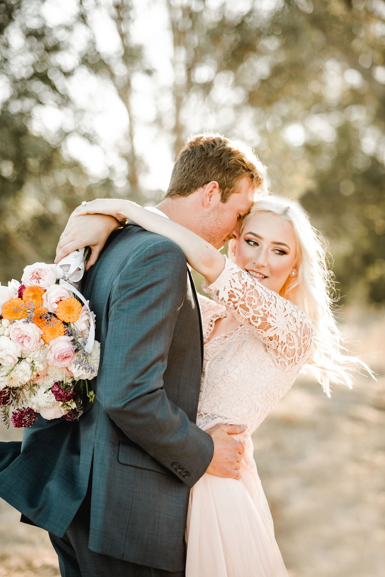 Wedding couple embracing in sunlit field with colorful bouquet.