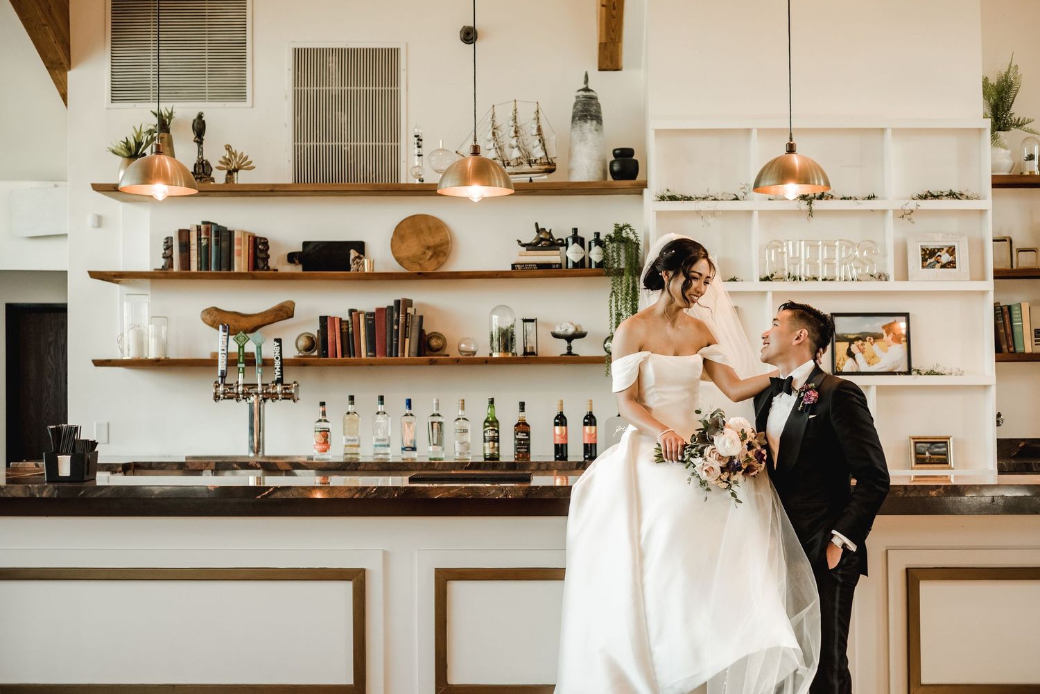 A couple shares an intimate moment at a stylish bar with floating wooden shelves and copper pendant lights.