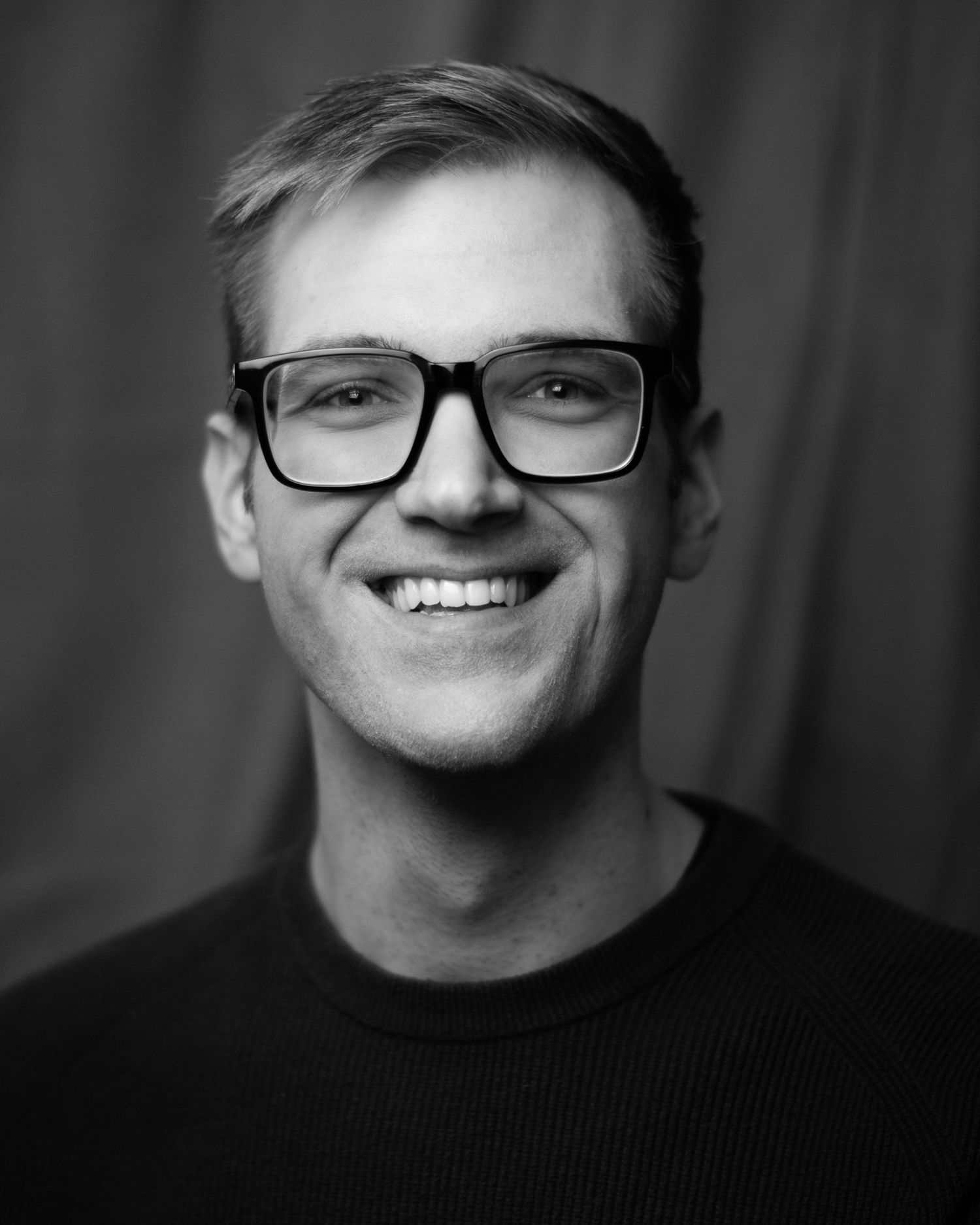 Black & White portrait image of a client from for a headshot session. A jolly look with glasses on, square on to the lens