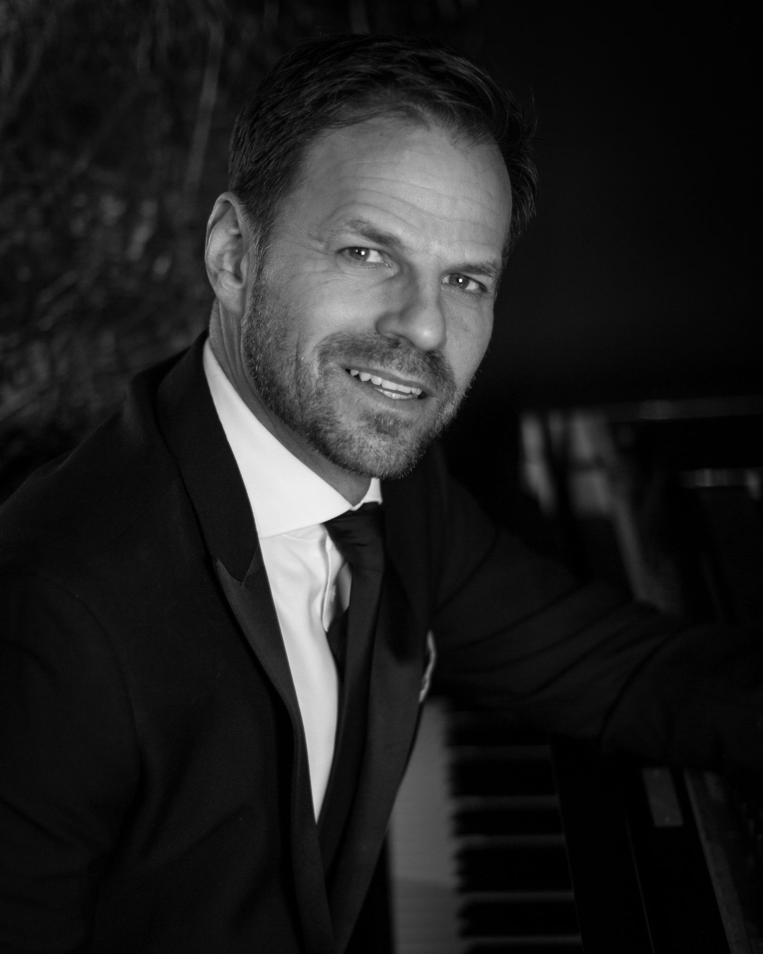 Black and white image of one of our clients leaning against a piano, part of our 'Swing into Spring' series for Ben Richards.