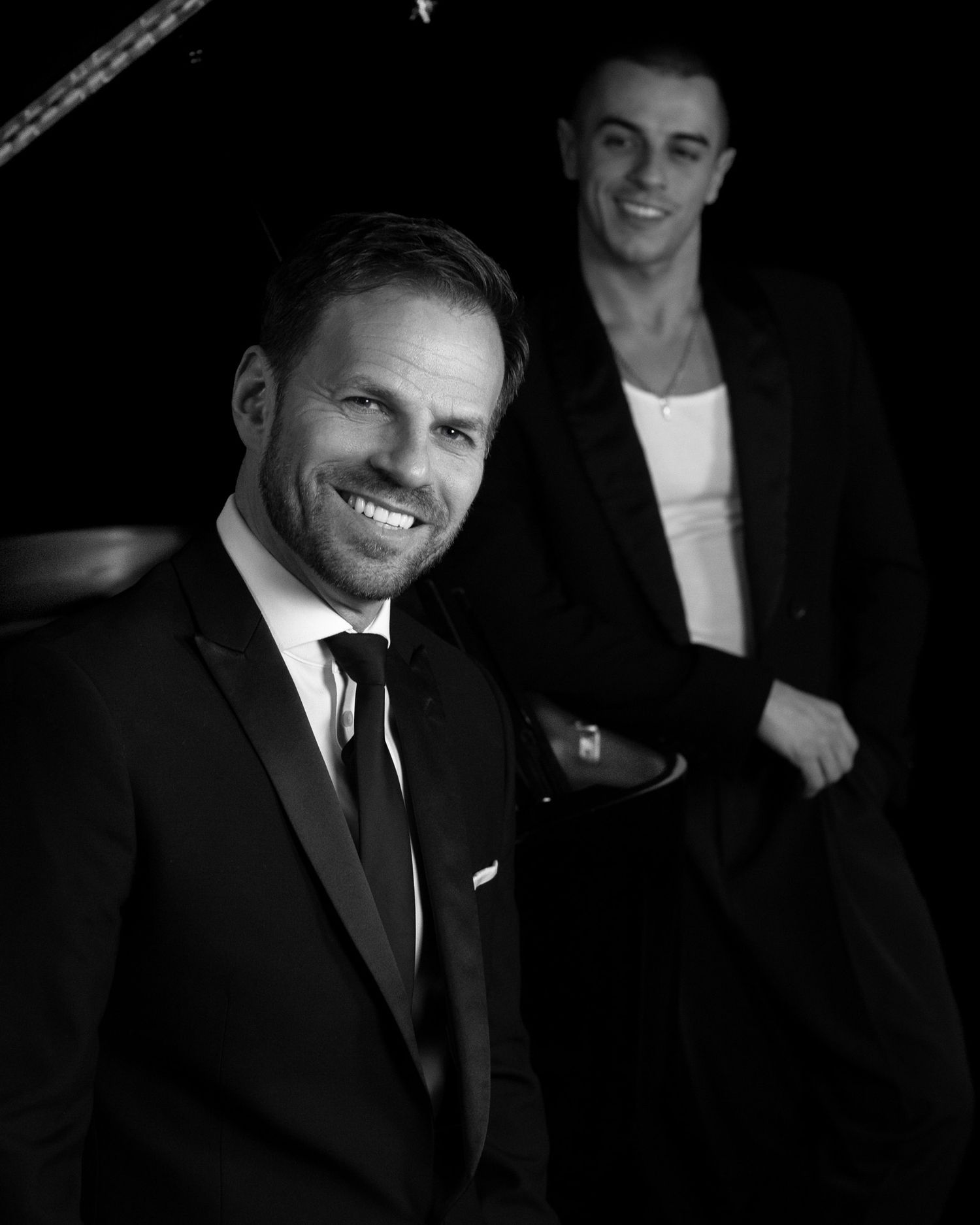 Black and white image of two of our clients leaning against a piano, part of our 'Swing into Spring' series for Ben Richards.