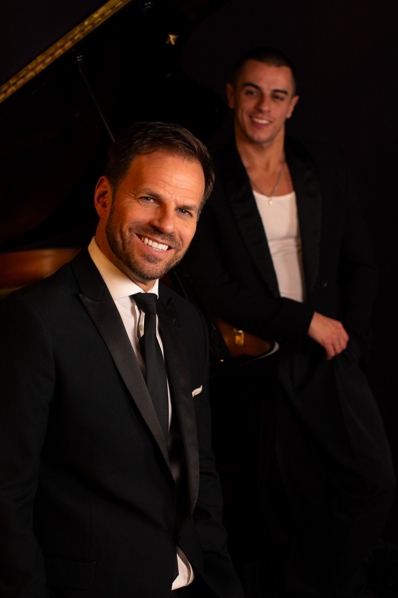 Colour image of two of our clients leaning against a piano, part of our 'Swing into Spring' series for Ben Richards.