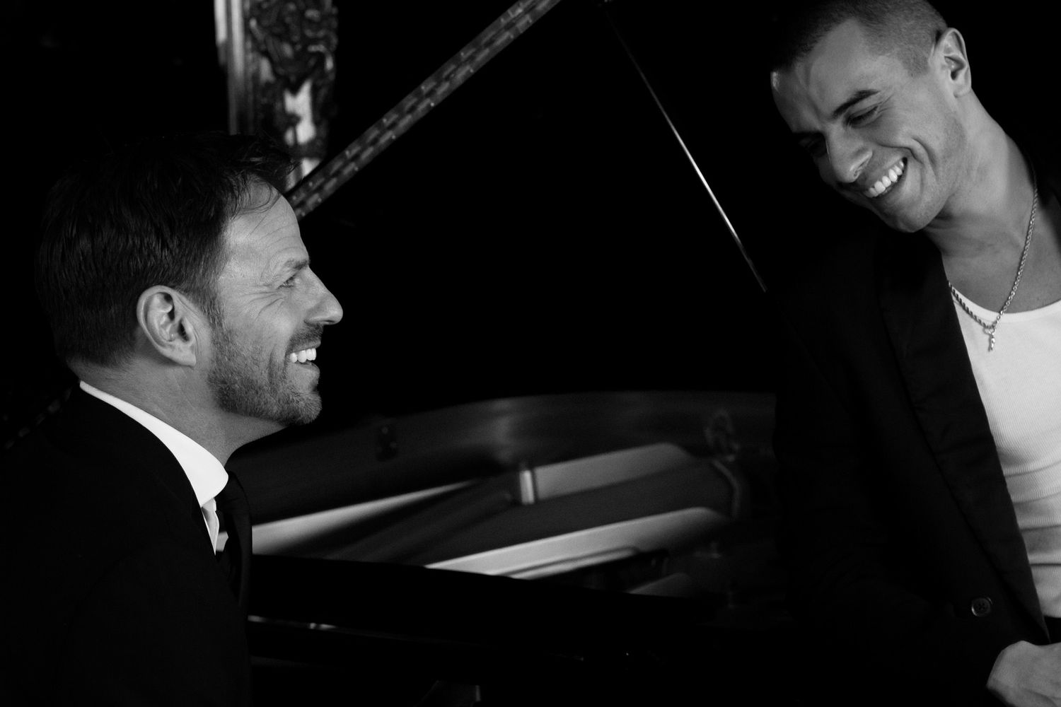 Black and white image of two of our clients leaning against a piano, part of our 'Swing into Spring' series for Ben Richards.