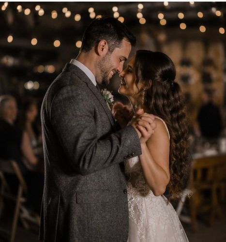 Bride and groom sharing first dance under warm string lights at romantic indoor wedding reception.