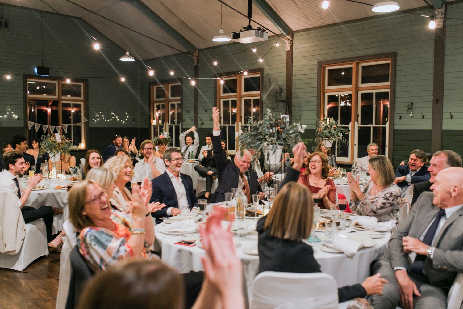 Rustic indoor reception setup with round tables near the water at Q Station Manly.
