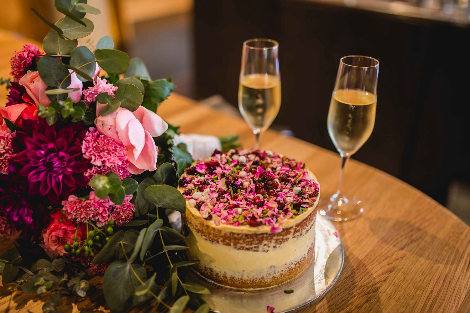 A rustic naked-style wedding cake decorated with fresh edible petals.
