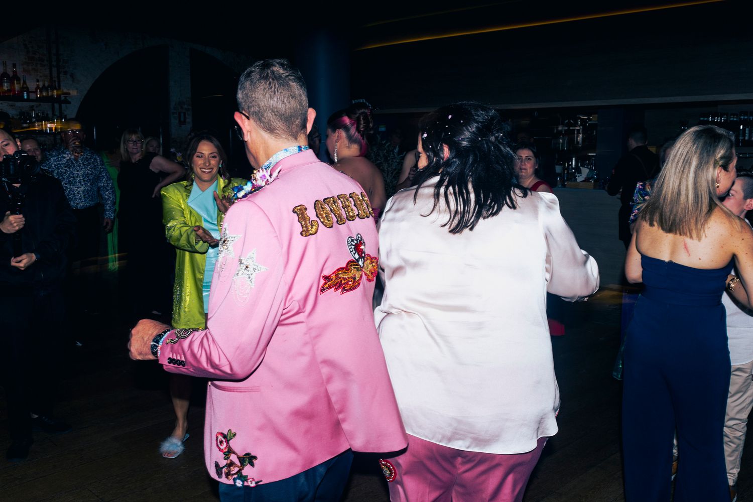 Guests dressed in extravagant Met Gala theme attire celebrating on the dance floor.