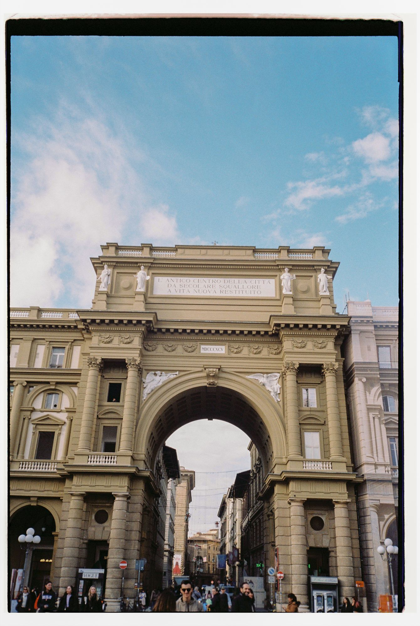Historic stone archway entrance to Flinders Street Station in Melbourne against a blue sky with white clouds.