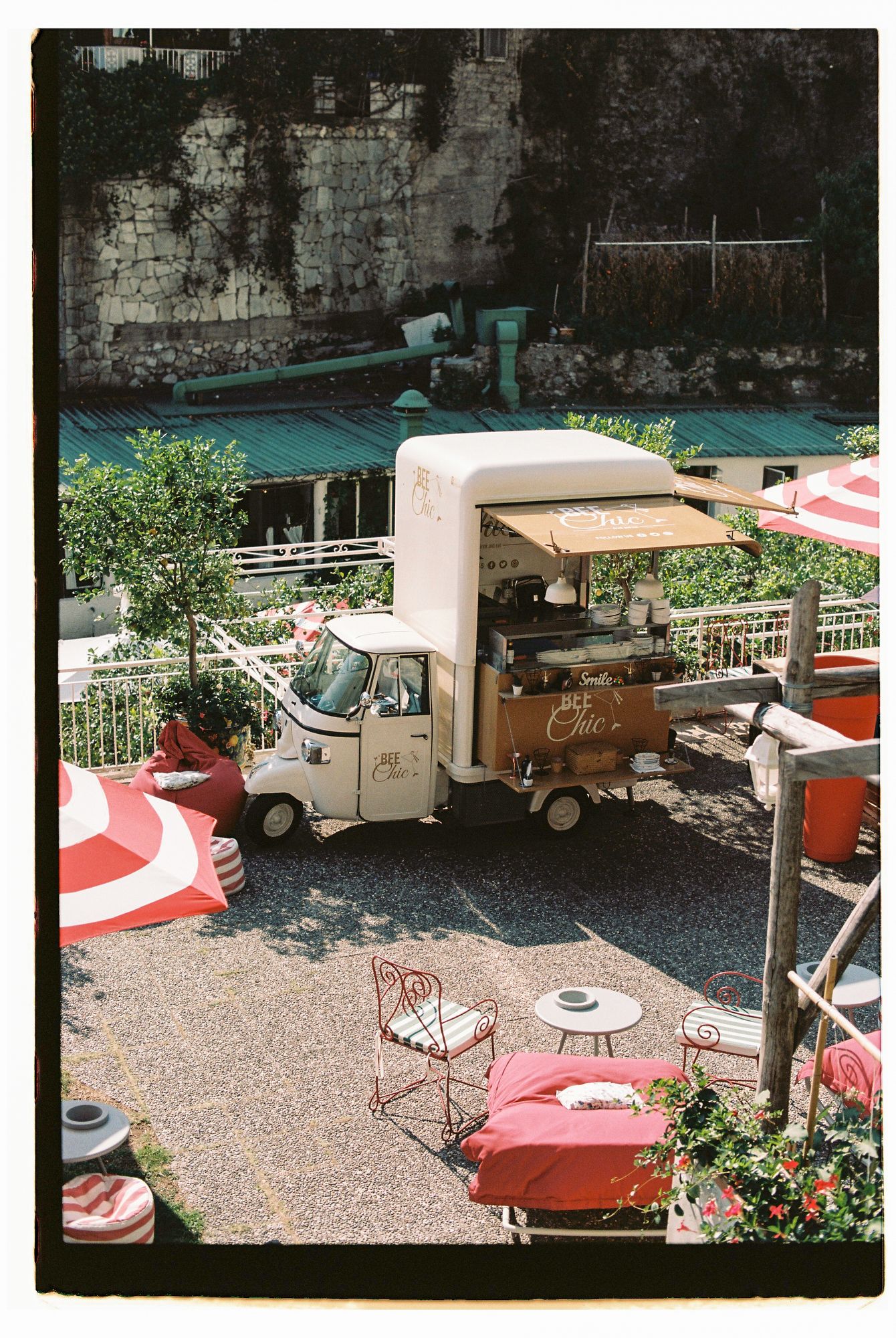 Vintage food truck parked in a gravel lot with outdoor seating and red and white barriers creating a dining area.