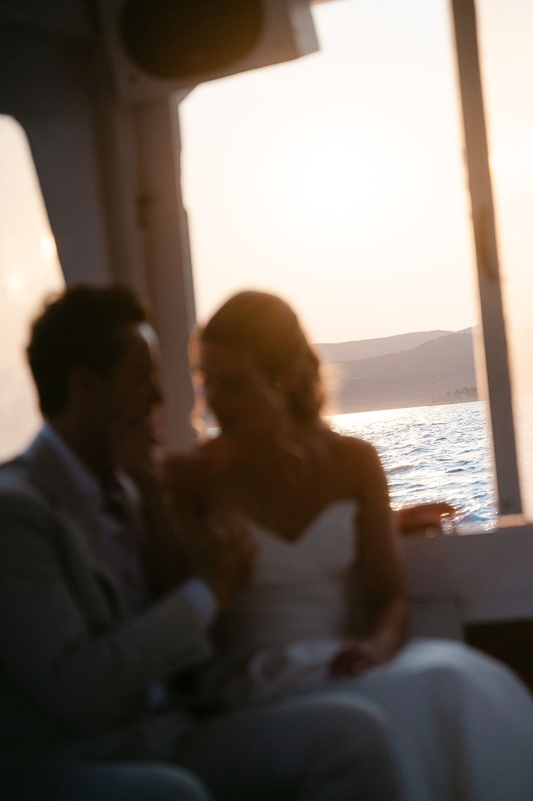 Silhouettes of people gathered on a boat deck at sunset with ocean view through windows at Poros