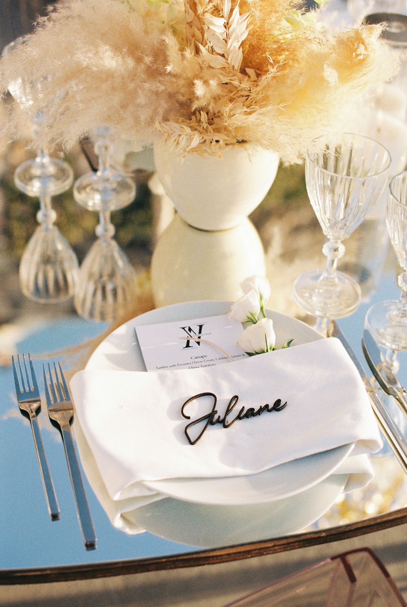 Elegant place settings with white napkins and name cards on a table decorated with crystal glassware and soft lighting.