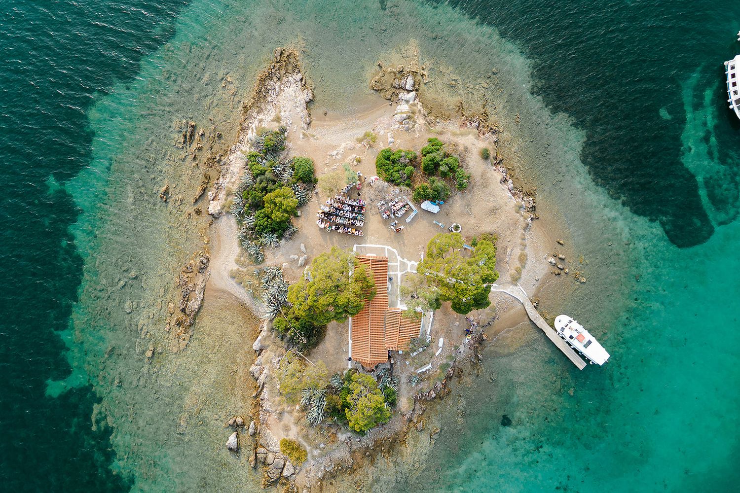 Aerial view of small rocky islands with boats anchored in crystal clear turquoise Mediterranean waters at Poros