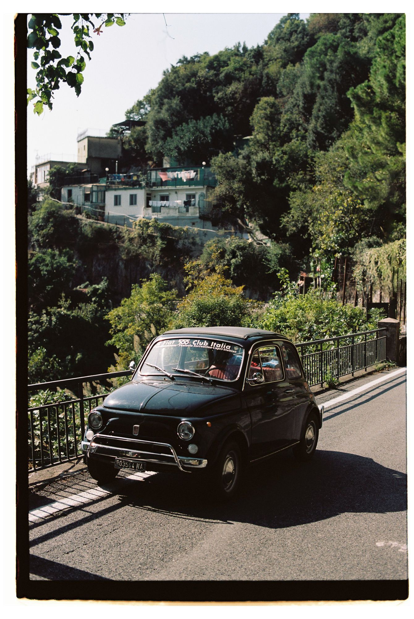 A black vintage VW Karmann Ghia parked on a hillside street with trees and buildings in the background at Amalfi