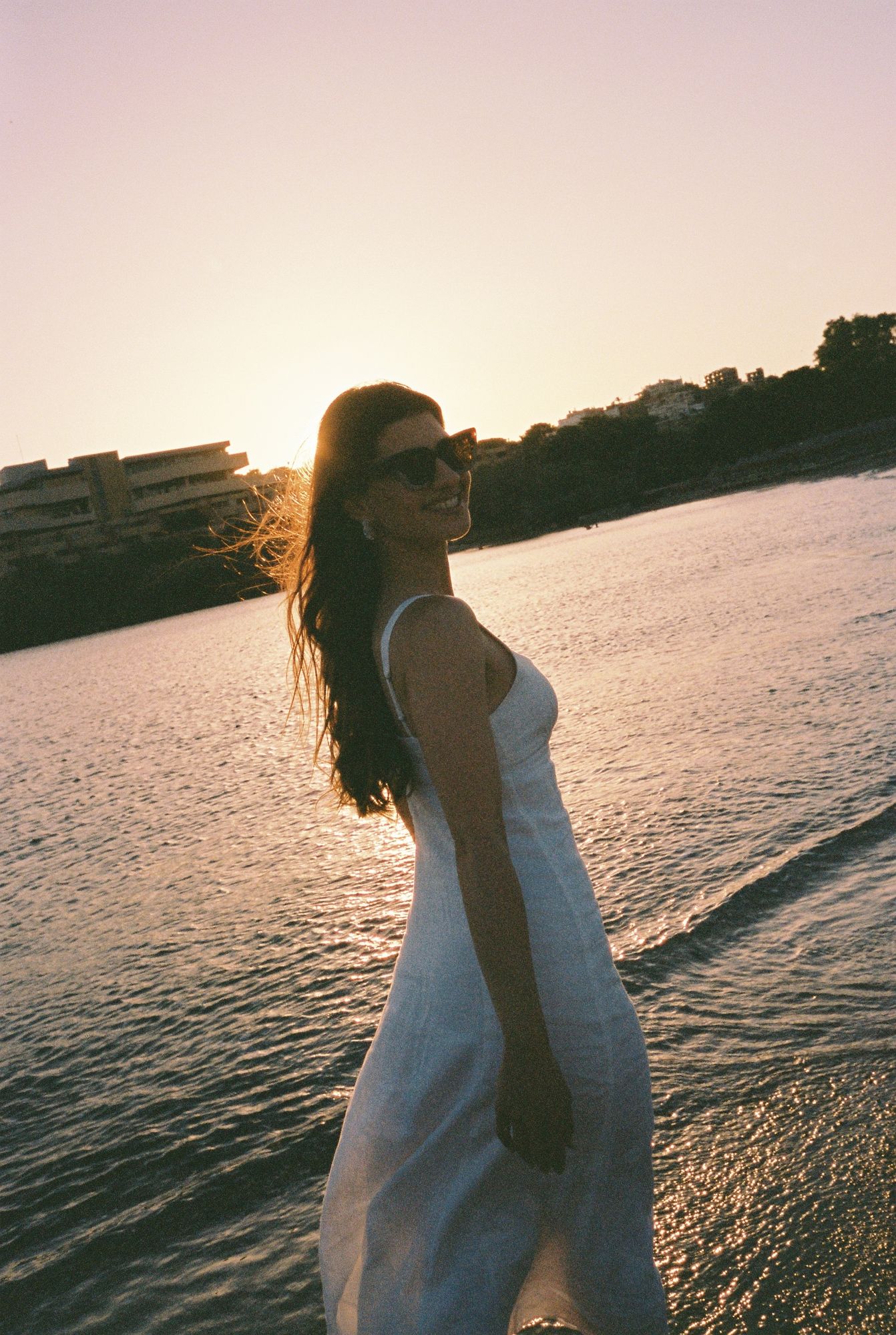 A series of romantic sunset silhouettes by the water showing a couple embracing in white attire against golden light on film