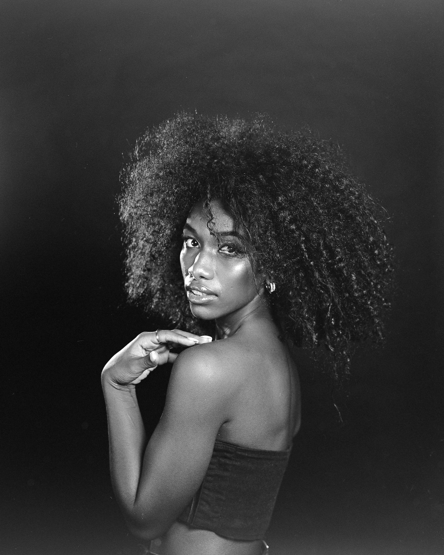 Black and white portrait series showing a figure with natural curly hair in expressive poses against a dark background.