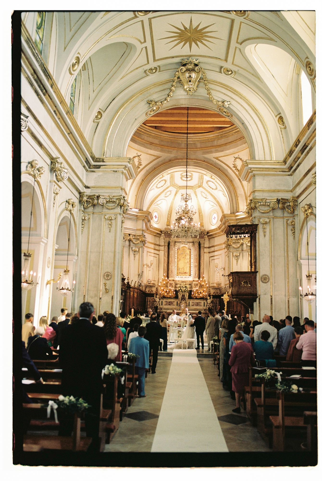Panoramic sequence showing the interior of an ornate baroque church with white and gold decor during a religious service.