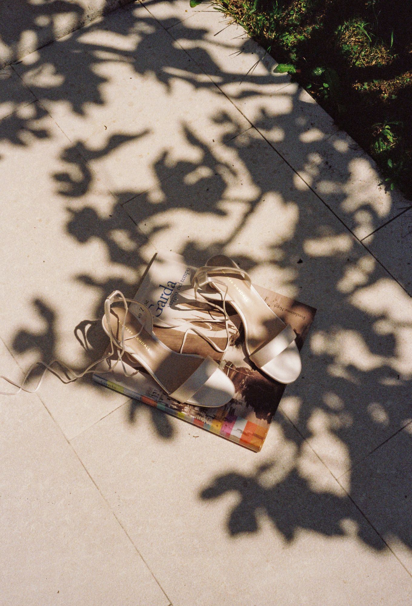A pair of beige lace-up sandals sits on a light floor with dappled tree shadows creating artistic patterns.