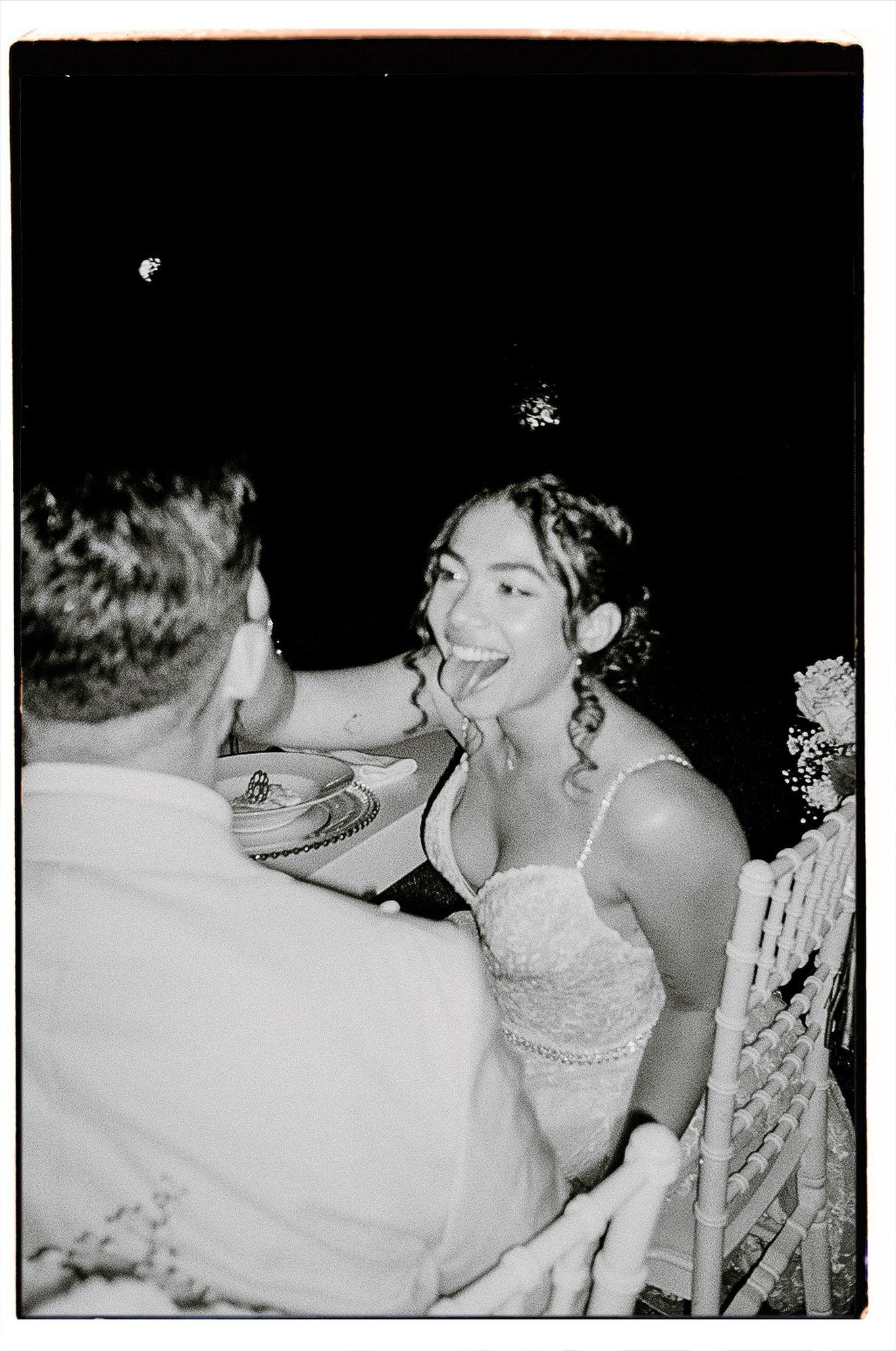 A black and white candid photo of a couple at a wedding reception sharing a joyful moment together.
