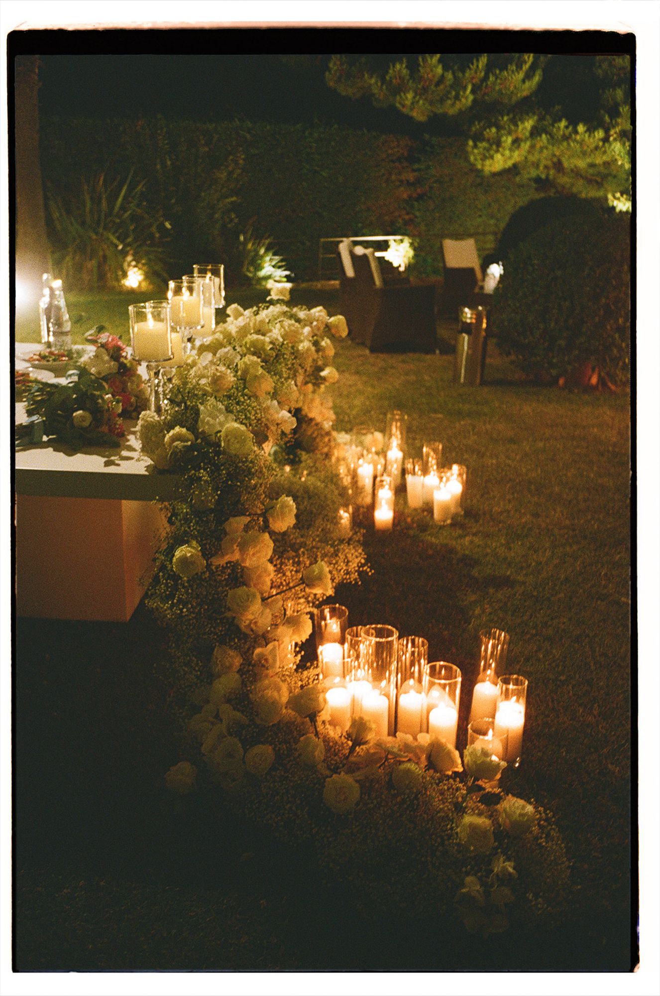 Romantic outdoor wedding reception setup with glowing candles and floral arrangements creating a warm ambiance in evening light on film