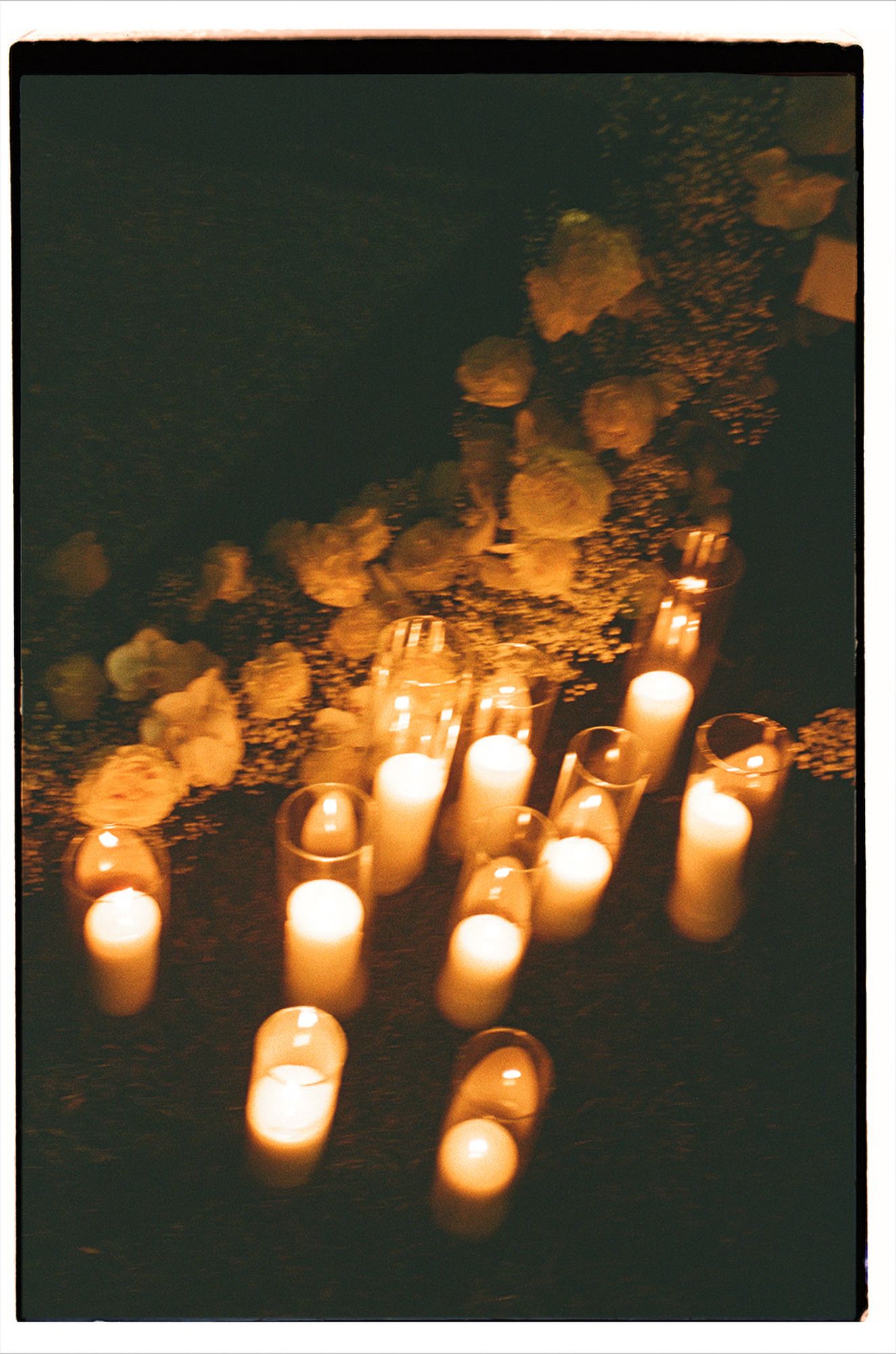 Multiple glowing candles in glass holders create a warm, atmospheric display against a dark background.