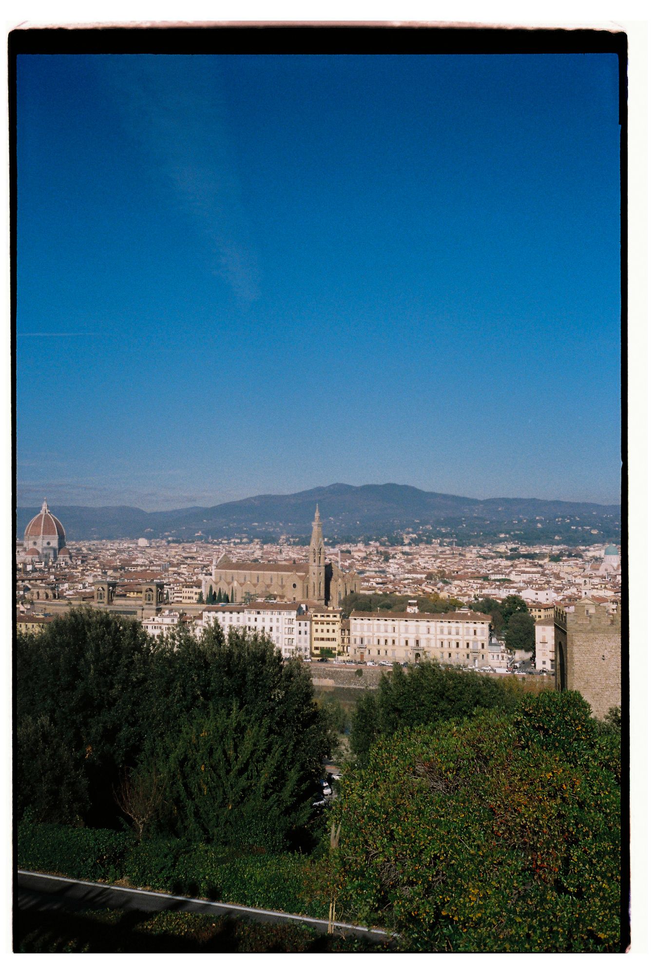 Panoramic view of Florence's historic skyline with the Duomo and surrounding architecture against blue skies and mountains.