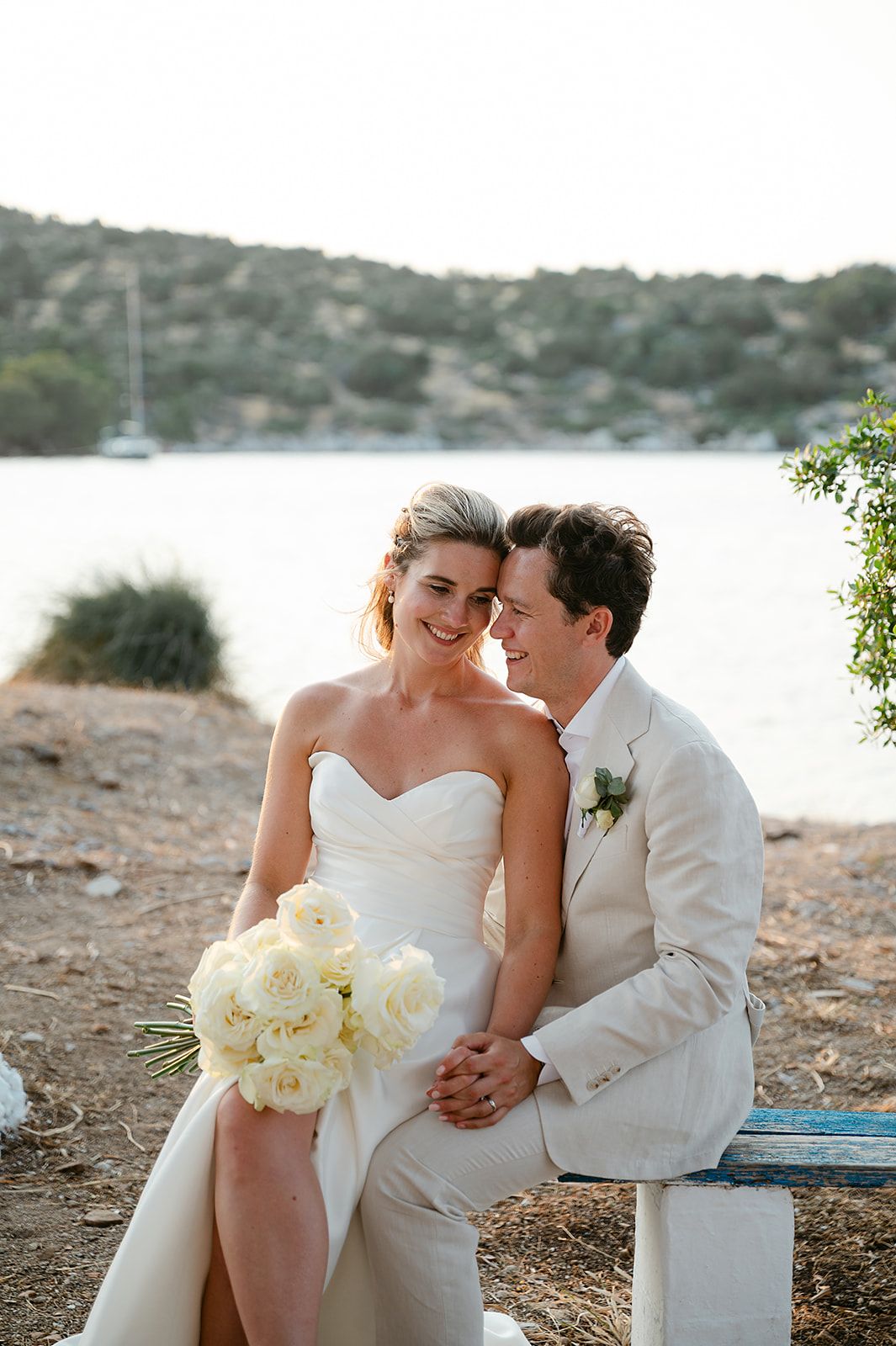 A couple in wedding attire shares an intimate moment by the waterfront on their special day at Poros