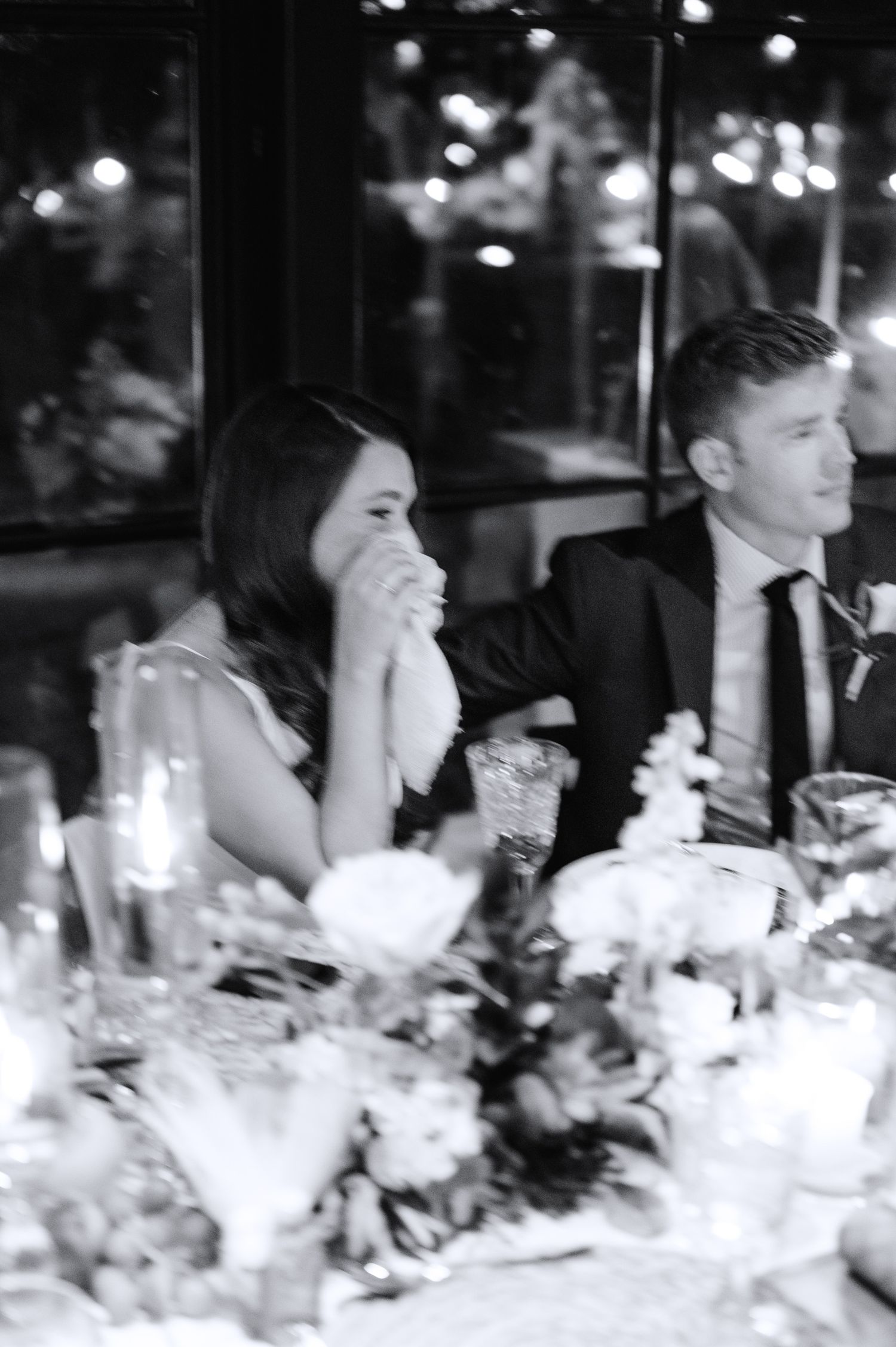 A black and white wedding reception scene with elegant floral centerpieces and guests seated at a formal dining table.