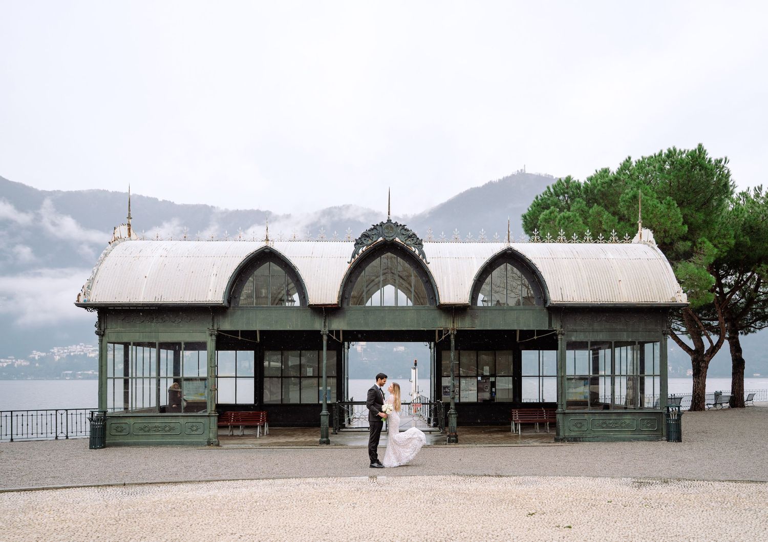 A panoramic view of beachfront buildings with green roofs along a sandy shoreline on a cloudy day at lake Como