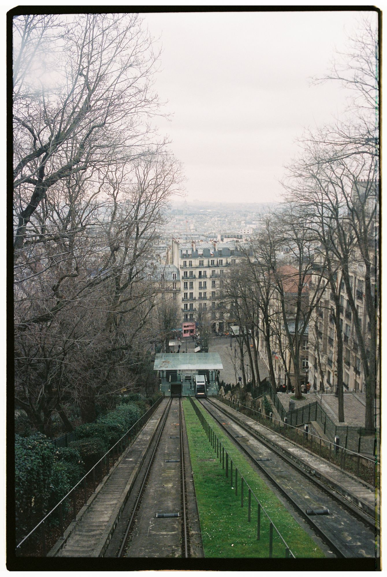 Funicular railway tracks lead down a steep hill in Montmartre Paris with bare winter trees and historic buildings on both sides.
