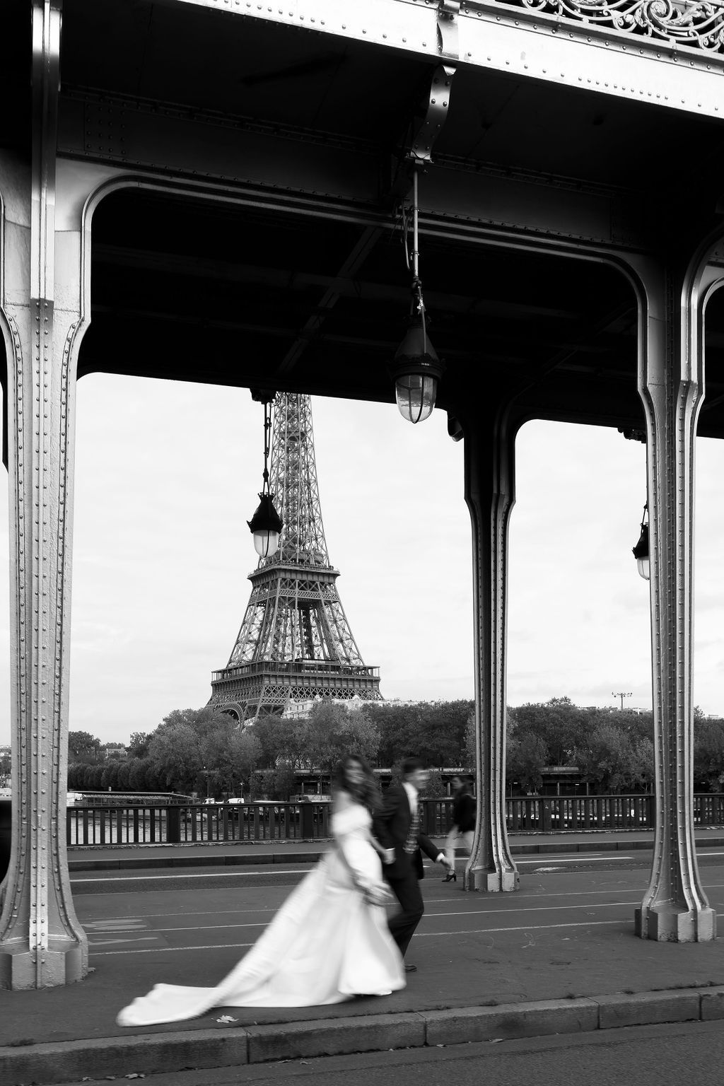 Black and white photo of a bride and groom walking on Bir-Hakeim Bridge with the Eiffel Tower in Paris, France.