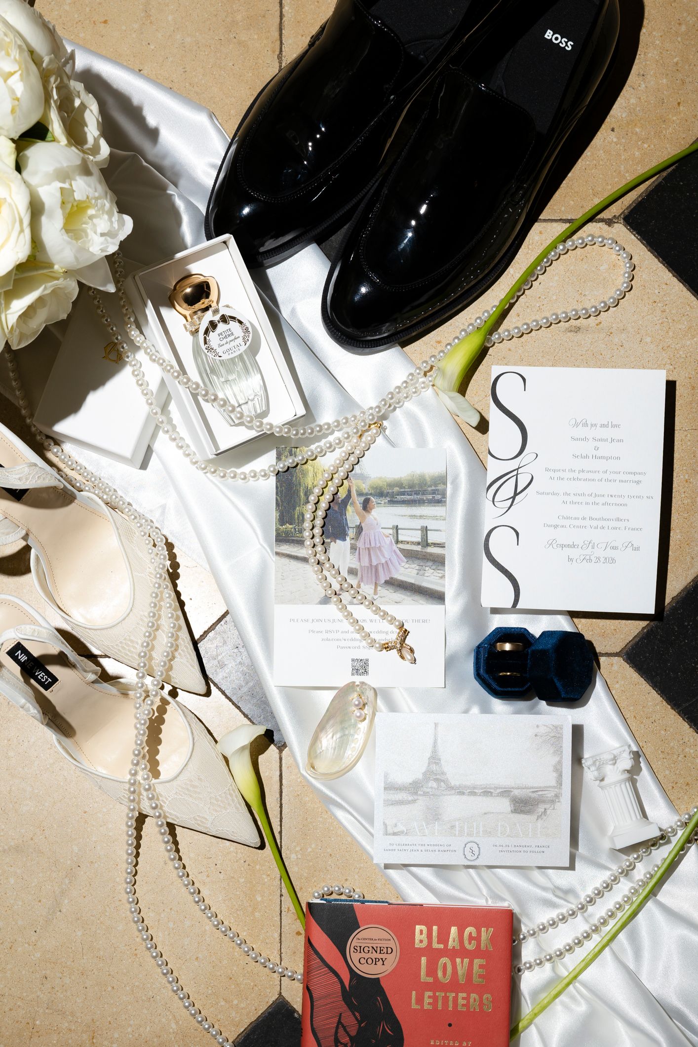 Elegant wedding flat lay featuring BOSS loafers, pearl jewelry, floral bouquet, invitations, and Black Love Letters book.