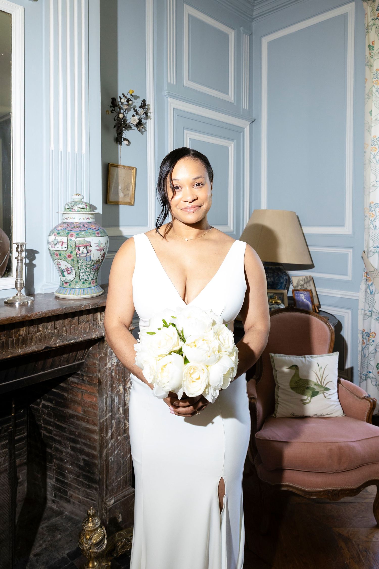 Bride in white gown holding bouquet of white roses in elegant blue French chateau room.