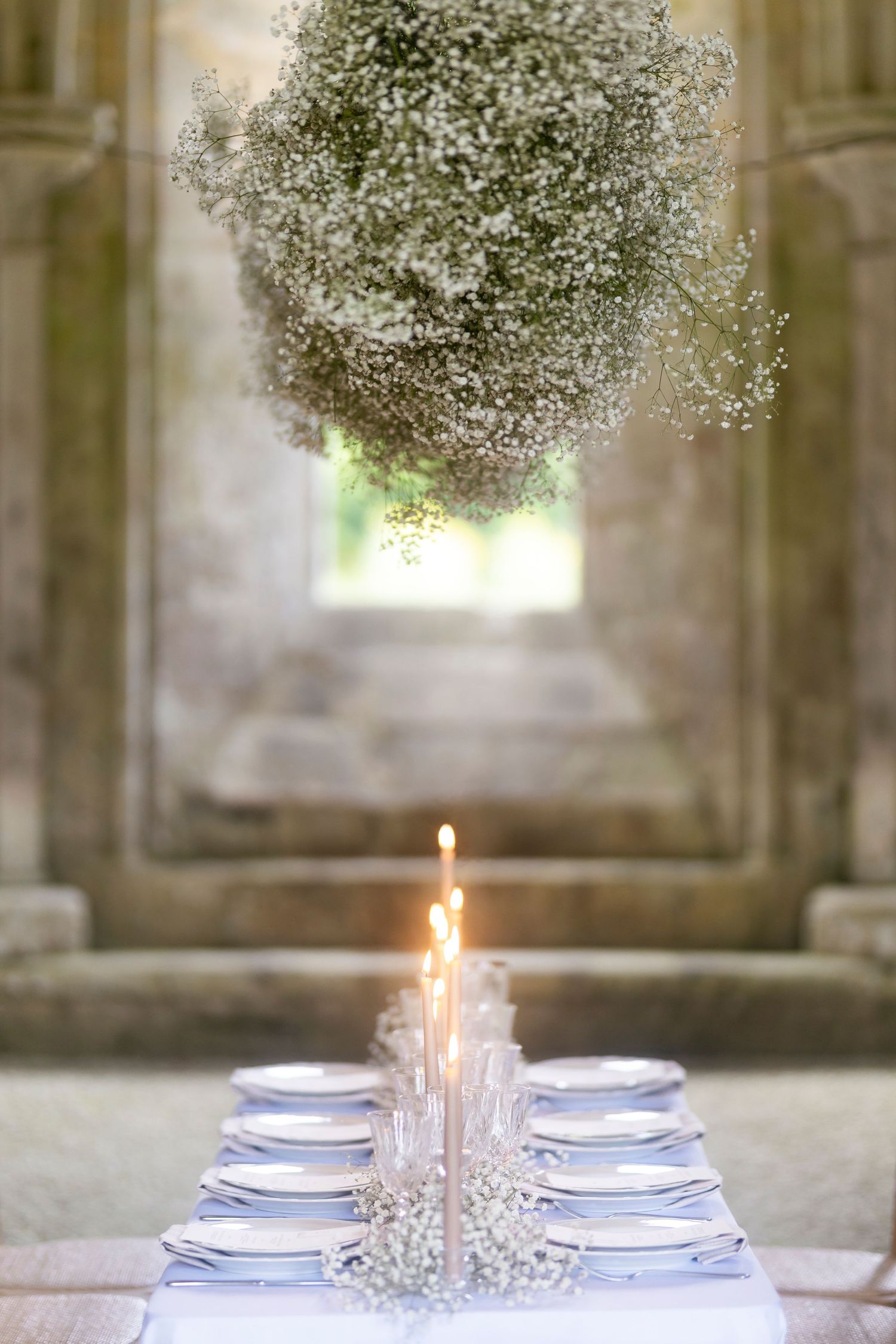 Elegant wedding table set with candles and baby's breath, beneath a floral cloud installation in a stone venue. wedding