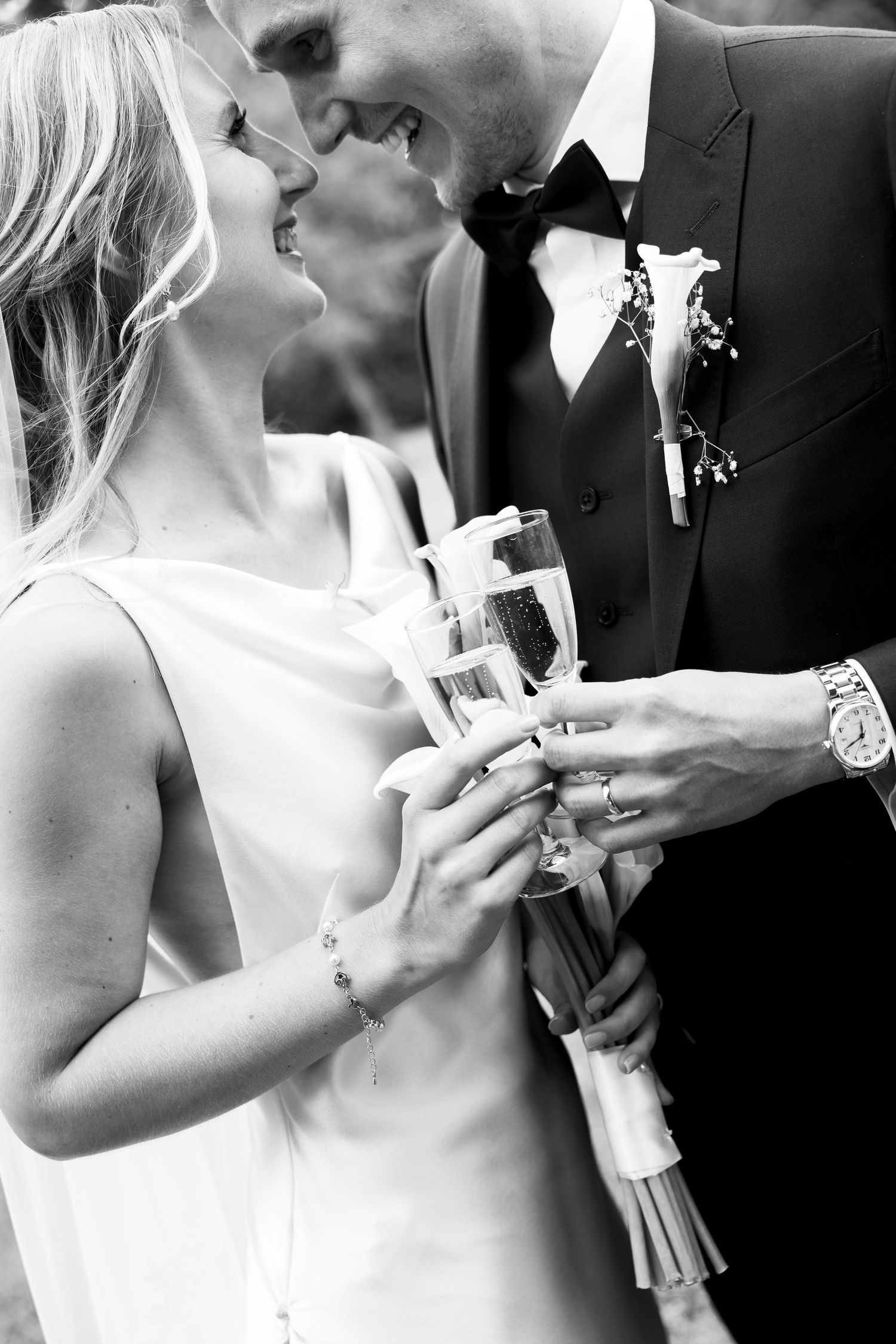 Black and white photo of a bride and groom sharing a kiss while holding champagne glasses on their wedding day.