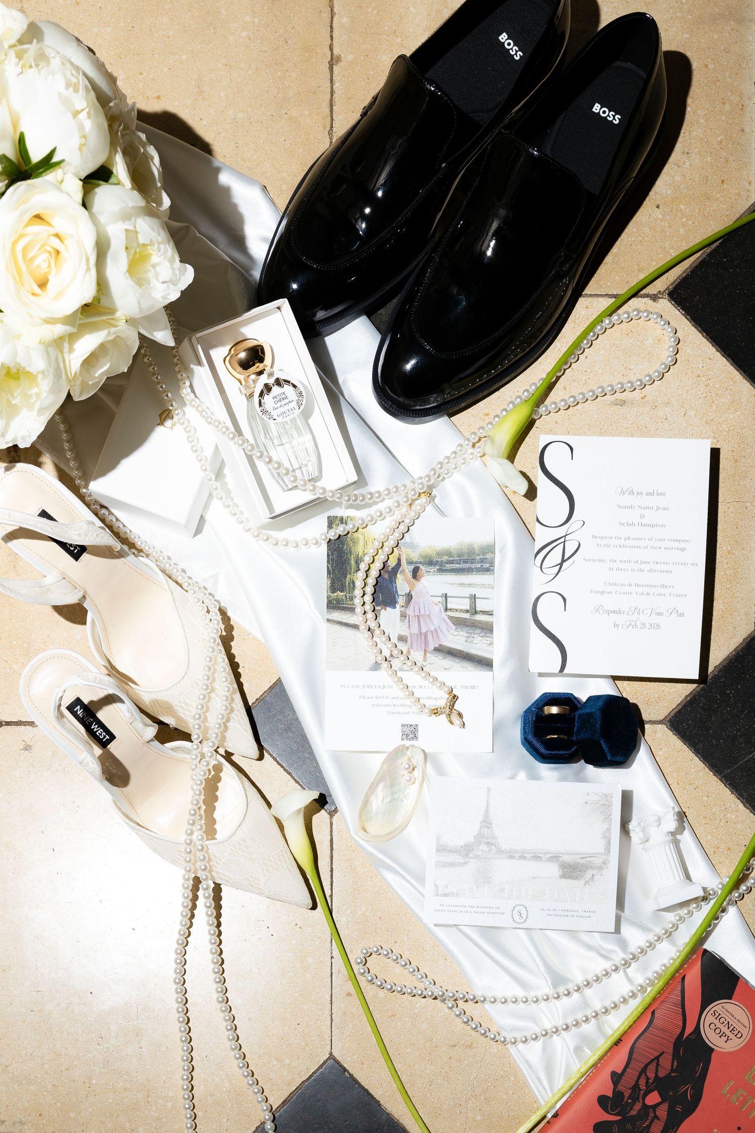 Elegant wedding flat lay featuring BOSS shoes, pearl necklace, white roses, perfume, rings, and wedding invitations . wedding photographer