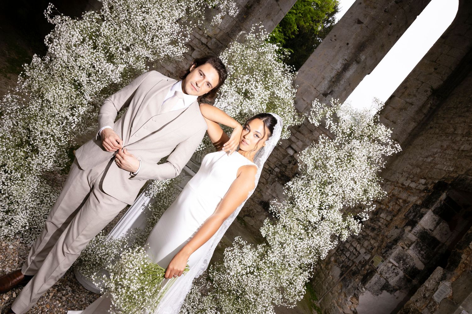 Bride and groom posing together outdoors surrounded by white baby's breath flowers at their wedding celebration.