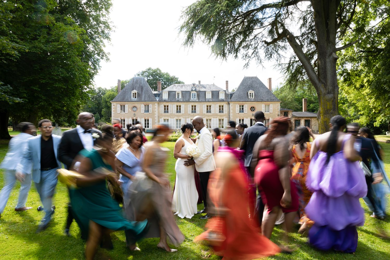 Guests dance joyfully on the lawn of an elegant French chateau during an outdoor wedding celebration.