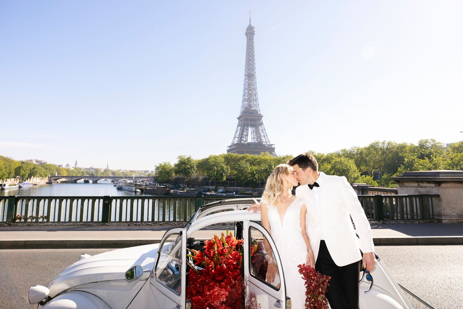 Couple kissing beside a vintage white car with red roses, Eiffel Tower and Seine River in background, Paris wedding.