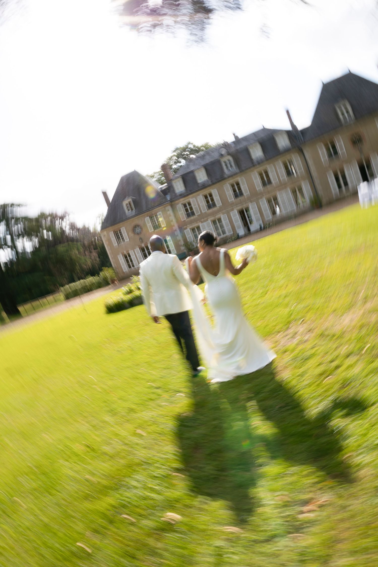 Bride and groom walking hand in hand across lawn toward grand French chateau.