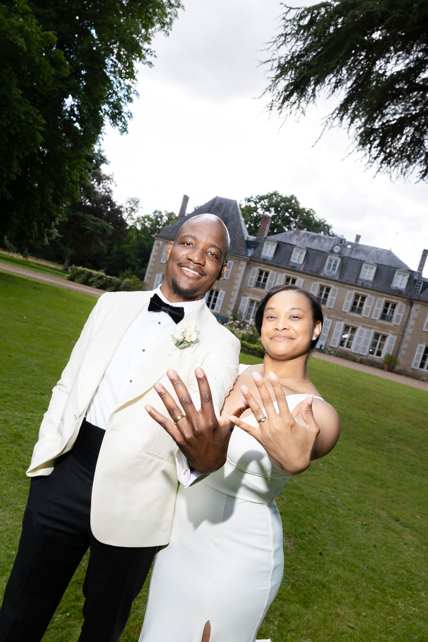 Newlywed couple in wedding attire showing off rings outside a French chateau on their wedding day. wedding photographer