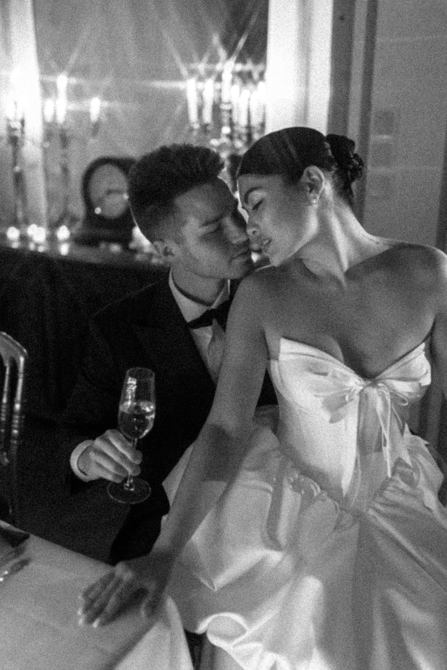 Black and white photo of a couple in wedding attire sharing an intimate moment, groom holding champagne glass.
