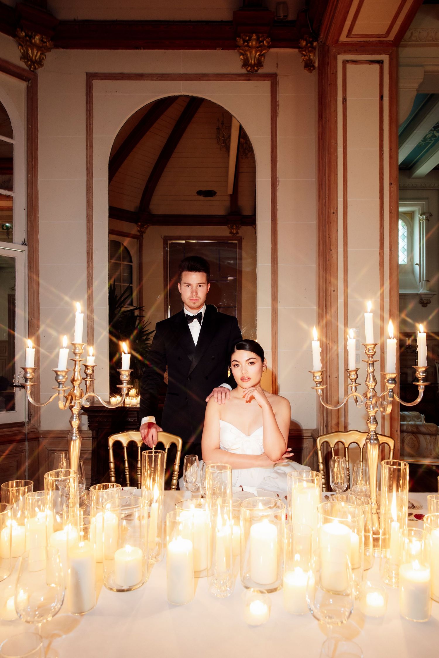 wedding photographer Elegant wedding couple seated at candlelit reception table with candelabras and champagne flutes in ornate venue.