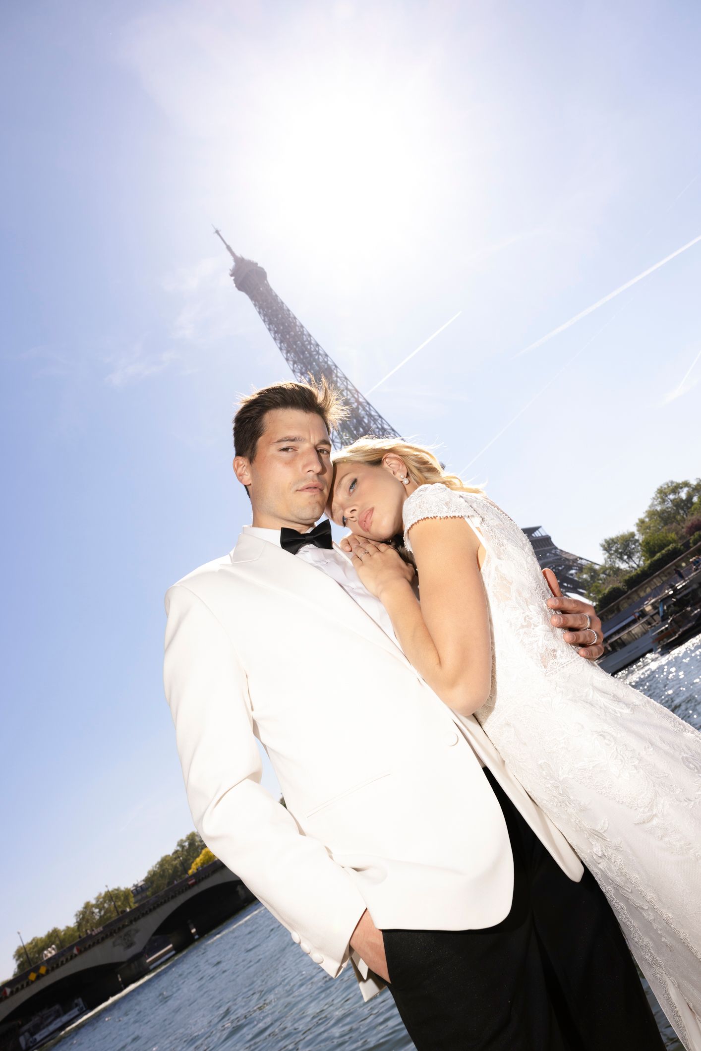 Newlywed couple embracing in front of the Eiffel Tower in Paris, groom in white tuxedo, bride in wedding dress.