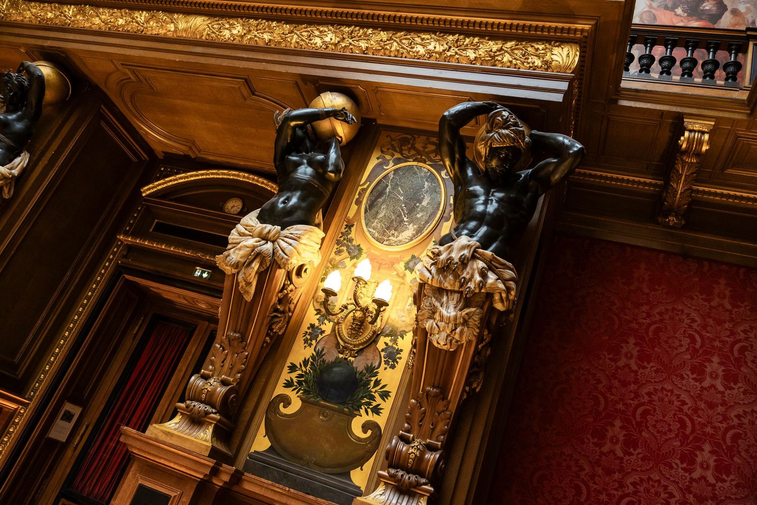 chateau de ferrieres Ornate golden clock flanked by bronze figures in an opulent gilded interior with red walls.