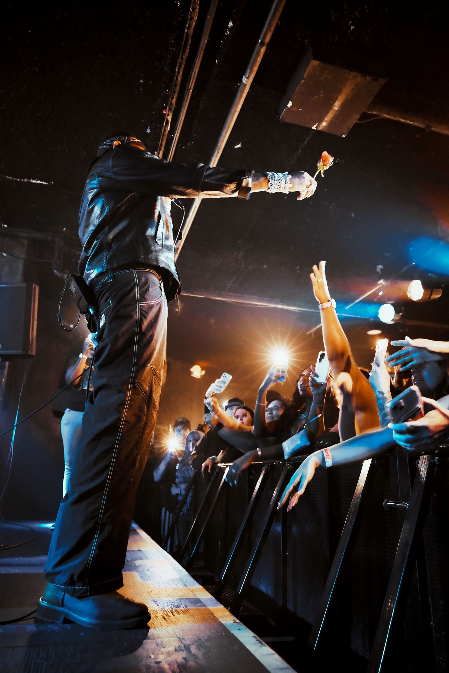 Performer on stage reaches out to excited crowd at a live concert venue with dramatic lighting.